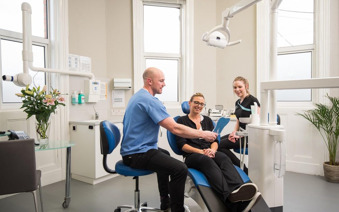 Dentista e assistente in uno studio moderno mentre spiegano una procedura a una paziente sorridente, simbolo di cura dentale e impianti dentali.